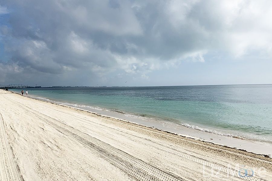 Large white sand beach front area with clouds over looking the dark blue ocean