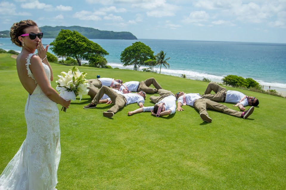 bride standing on the golf course for the bouquet and groomsmen are on the ground with the ocean in the background