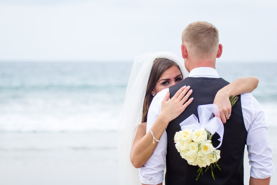 briding groom in bracing by the ocean with the bride holding a bouquet of yellow flowers