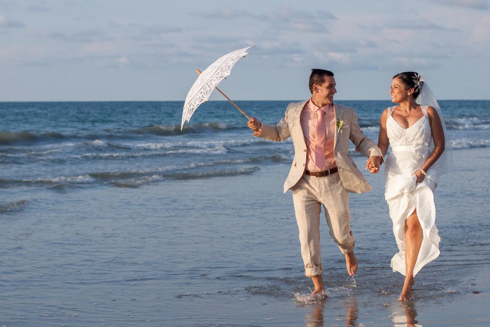 wedding couple with groom holding on Bralla while walking through the water in the ocean