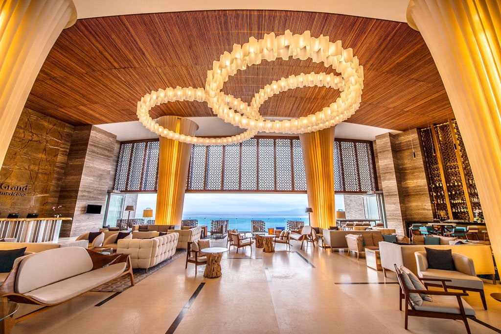 main lobby area with a beautiful chandelier lighting white couches and white chairs with a view of the ocean