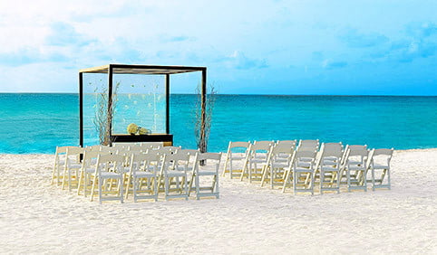 Beautiful gazebo set up by the ocean with the white chairs and beautiful Decor