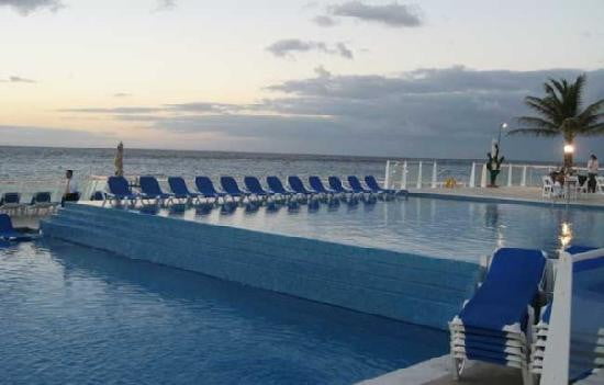 Main pool with blue lounge chairs surrounding it and ocean at sunset